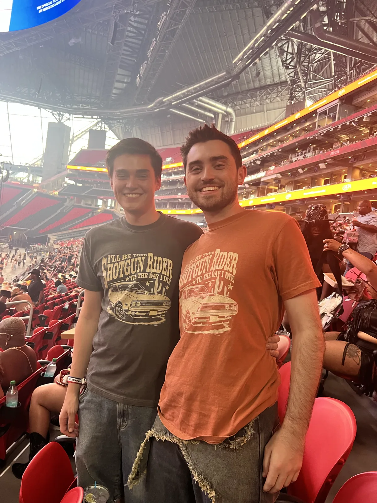 Wesley Chandler and Sam smiling together in matching graphic T-shirts at a stadium