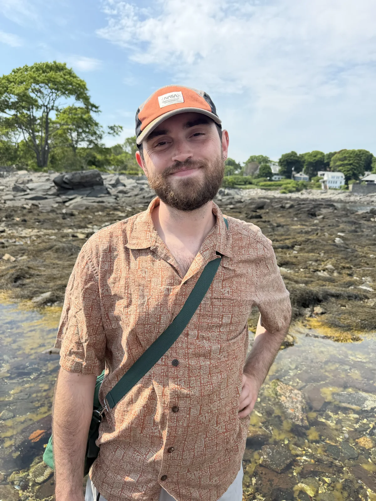Wesley Chandler smiling on a rocky shoreline in an orange cap and patterned shirt